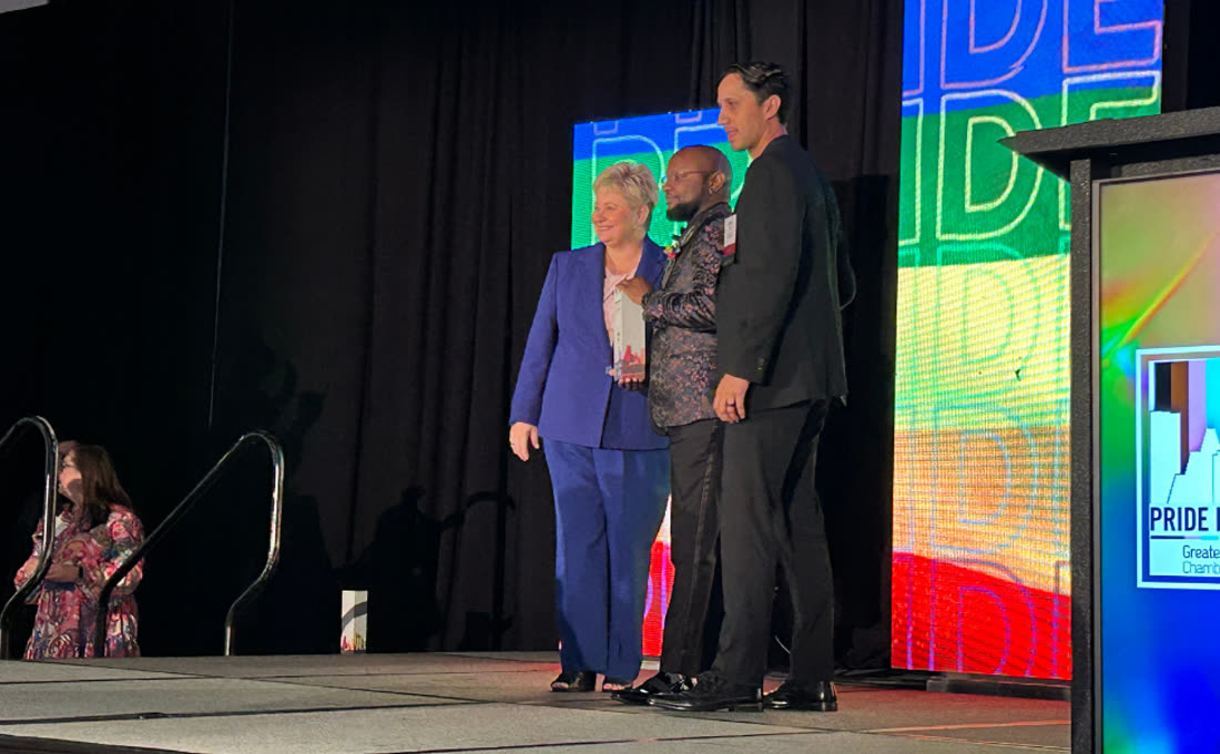 Liam J. Adair receiving the LGBTBE Certified Business of the Year award on stage from Tammi Wallace, Co-Founder, President and CEO of the Greater Houston LGBT Chamber of Commerce, with presenter Jason Rocha, 2023