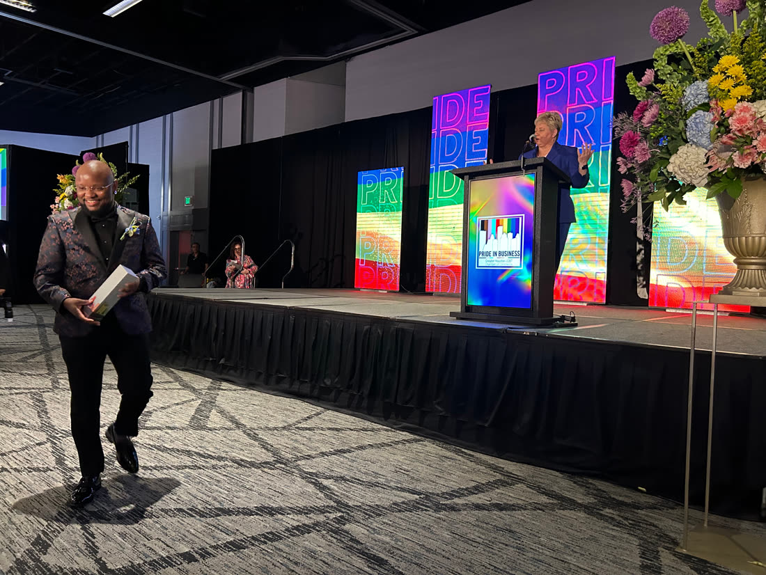 Liam J. Adair walking off stage holding the LGBTBE Certified Business of the Year award at the Pride in Business Awards, 2023